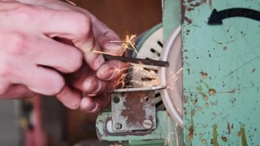 Metal bir parçayı ağır çekimde işlemekten parlak kıvılcımlar çıkıyor. Elektrikli öğütme çarkında metal öğütme, yakın plan. Bir atölyede aşındırıcı bir tekerlek üzerinde çalışan bir zanaatkarın elleri..