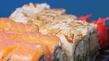Suşi plastik bir kutuda yuvarlanır ve yakın plan çekilir. İçinde taze Japon dürümleri, zencefil ve vasabi olan suşi kutusu teslimat plastik bir kapta dönüyor. Asya yemekleri, paket yemek, sağlıklı yemek.
