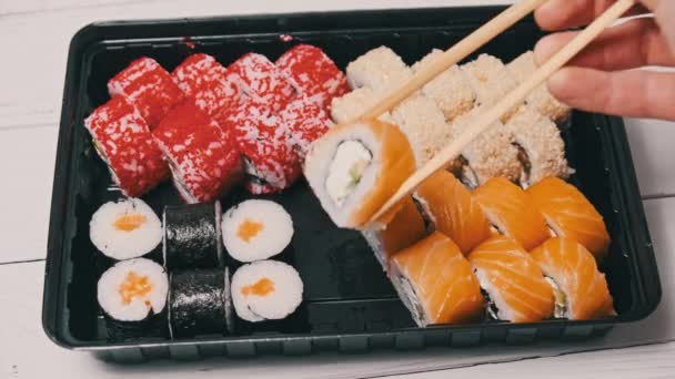 筷子从寿司盒里取出一个寿司 在塑料盒里打滚 日本的一套各种美味的寿司卷在一个运送容器里 亚洲概念食品 健康食品 外卖食品 — 图库视频影像