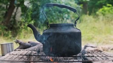 Eski çaydanlık doğada bir turist kamp ateşinin üzerinde duruyor. İs dumanı ile kararmış çaydanlık, yerdeki taşlardan yapılmış kendi kendini yetiştirmiş turist ocağının üzerinde kaynıyor. Açık ateşte çay yapmak.