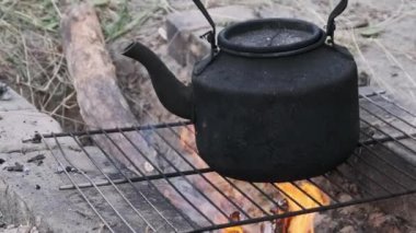 Eski çaydanlık doğada bir turist kamp ateşinin üzerinde duruyor. İs dumanı ile kararmış çaydanlık, yerdeki taşlardan yapılmış kendi kendini yetiştirmiş turist ocağının üzerinde kaynıyor. Açık ateşte çay yapmak.