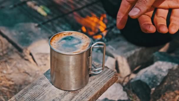 在大自然的篝火上准备自酿的香浓咖啡 在篝火的特写下 带着香浓咖啡的游客杯 旅行者的手拿着一个刚烤好的咖啡杯 徒步旅行 — 图库视频影像