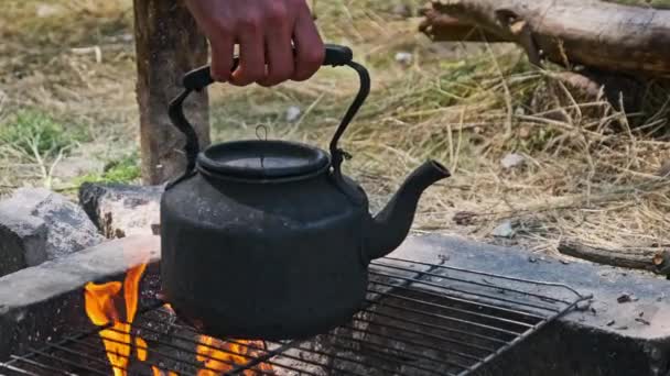 一个烟雾腾腾的水壶是用石子铺在地面上的自制旅游炉上的开水 一个游客从火中抢了一个茶壶 古老的水壶矗立在自然的旅游篝火上 — 图库视频影像