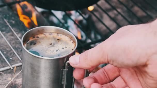 在大自然的篝火上准备自酿的香浓咖啡 在篝火的特写下 带着香浓咖啡的游客杯 旅行者的手拿着一个刚烤好的咖啡杯 徒步旅行 — 图库视频影像