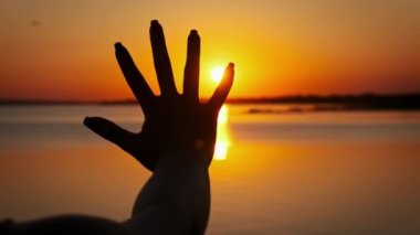 Siluet kadın eli gün batımına doğru uzanıyor, ağır çekimde. Avuç içi açık kadın avuçlarının arasına güneş ışınları yerleştiriyor. Kollar güneşe, inanç Tanrı 'ya. Hayal, mutluluk, özgürlük, zihinsel sağlık.