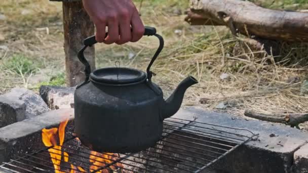 煤烟水壶是用石子铺在地面上的自制旅游炉上的开水 一个游客从火中抢了一个茶壶 古老的水壶矗立在自然的旅游篝火上 — 图库视频影像