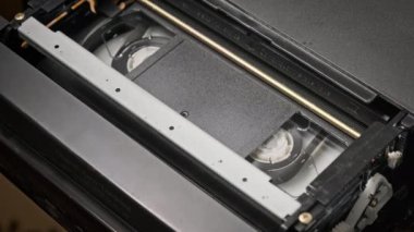 VHS kaset bir VCR kaydedicinin içinde oynatılıyor, üst görünümde. Video kaset makaraları dönüyor. Boş etiketli video kaset oynatmaya başlıyor. İçerideki eski video kaydedici. Eski filmi oynuyorum..