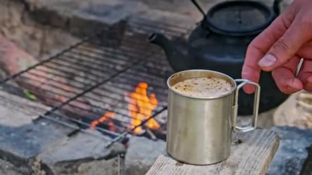 在篝火的特写下 带着香浓咖啡的游客杯 在大自然的篝火上准备自酿的香浓咖啡 旅行者的手拿着一个刚烤好的咖啡杯 徒步旅行 — 图库视频影像