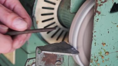 Metal bir parçayı ağır çekimde işlemekten parlak kıvılcımlar çıkıyor. Elektrikli öğütme çarkında metal öğütme, yakın plan. Bir atölyede aşındırıcı bir tekerlek üzerinde çalışan bir zanaatkarın elleri..