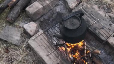 Eski çaydanlık doğada bir turist kamp ateşinin üzerinde duruyor. İs dumanı ile kararmış çaydanlık, yerdeki taşlardan yapılmış kendi kendini yetiştirmiş turist ocağının üzerinde kaynıyor. Açık ateşte çay yapmak.