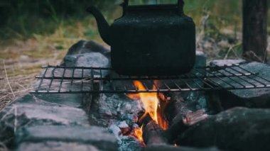 Eski çaydanlık doğada bir turist kamp ateşinin üzerinde duruyor. İs dumanı ile kararmış çaydanlık, yerdeki taşlardan yapılmış kendi kendini yetiştirmiş turist ocağının üzerinde kaynıyor. Açık ateşte çay yapmak.