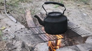 Ateşin üstünde çaydanlık. Eski model tütsülenmiş bir çaydanlık, yerdeki taşlardan yapılmış kendi kendini yetiştirmiş turist ocağının üzerinde kaynar su. Kampın yakınındaki ormanda şenlik ateşinde çay yapmak, yakın plan..