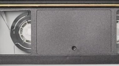 VHS kaset bir VCR kaydedicinin içinde oynatılıyor, üst görünümde. Videokaset makaraları dönüyor. Boş etiketli video kaset oynatmaya başlıyor. İçerideki eski video kaydedici. Klasik film oynatılıyor