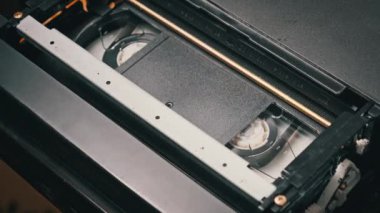 VHS video kasedi VCR kaydedicinin içine koyuldu ve oynatılıyor. Video kasetin klasik VHS mekanizması video başına bant takar. İçerideki eski video kaydedici. Eski video dosyası veya film çalma kavramı.