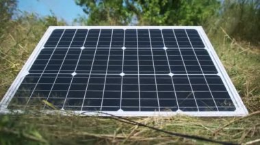 Taşınabilir güneş paneli doğada, yakın planda, yerde yatıyor. Turizm ve kamp alanları için güneş enerjisi. Çimenlerdeki bir güneş paneli güneşli bir yaz gününde enerji üretir. 4K