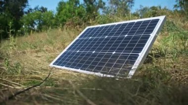 Taşınabilir güneş paneli doğada, yakın planda, yerde yatıyor. Turizm ve kamp alanları için güneş enerjisi. Çimenlerdeki bir güneş paneli güneşli bir yaz gününde enerji üretir. 4K