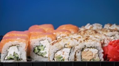 Yemek çubukları suşi kutusuna bir suşi koydu, yakın plan. Plastik bir kutuda yuvarlanıyor. Çeşitli lezzetli suşi setleri bir teslimat konteynerinde. Konsept Asya yemekleri, sağlıklı yiyecekler, paket yemek.