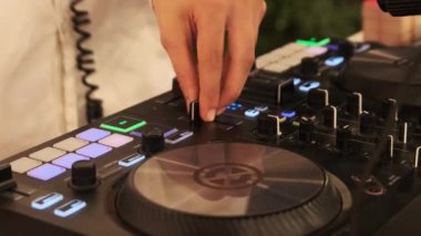 DJ gece partisinde DJ kumandayı kullanarak müzik çalar. Mikser konsolunda dans müziği karıştırıyorum. DJ elleri modern dijital düğmeleri, faders, jog tekerlekleri ve çok renkli aydınlatma düğmelerini kuruyor