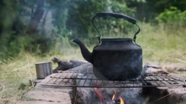 Tütsülenmiş çaydanlık, yerdeki taşlardan yapılmış kendi kendini yetiştirmiş turist ocağının üzerinde kaynar su. Doğada bir turist kamp ateşinin üzerinde duran eski bir çaydanlık. Ormanda şenlik ateşinde çay yapmak.