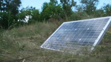 Taşınabilir güneş paneli doğada, yakın planda, yerde yatıyor. Turizm ve kamp alanları için güneş enerjisi. Çimenlerdeki bir güneş paneli güneşli bir yaz gününde enerji üretir. 4K