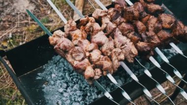 Şişte şiş kebaplar açık havada mangalda pişirilir. Kızarmış sulu domuz eti ızgaradaki metal şişte kızartılıyor, yakın plan. Yaz pikniğinde mangal kömürlü ve dumanlı. 4K