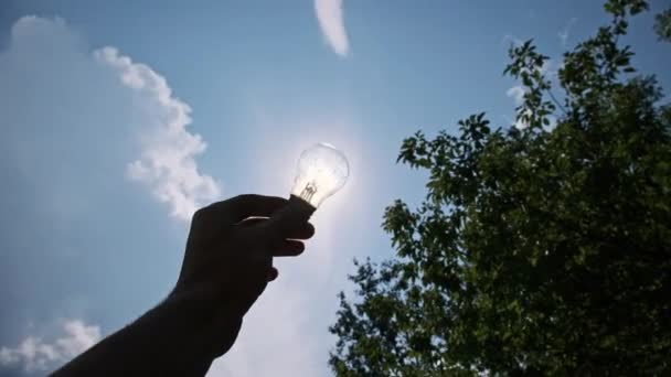 在明亮的太阳和蓝天的映衬下 一只雄性手的Pov轮廓手握着一个灯泡 老白炽灯泡和阳光太阳光穿过灯泡使它发光 可再生能源 — 图库视频影像