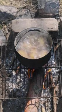 Dikey patatesler doğadaki bir kamp ateşinde tencerede suda pişirilir. Genç patateslerin çoğu, ocağın üzerinde kaynamış suda kaynatılır. Ormanda kamp yaparken yemek pişirmek.