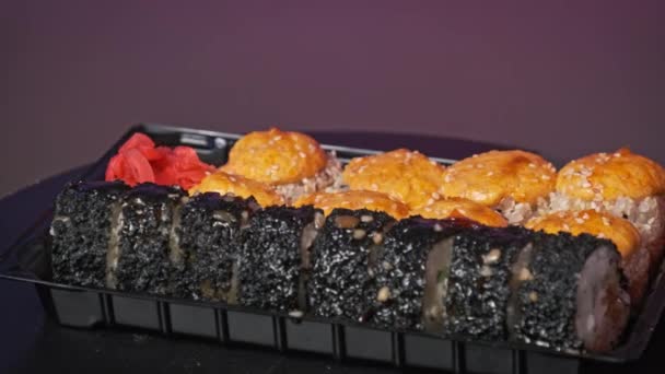 プラスチック製の箱の中で焼いた寿司ロールは クローズアップを回転させます 新鮮な日本のおいしいロールを配達容器に回転させて すぐに食べることができます 食品の配達 持ち帰りの食品の概念 — ストック動画