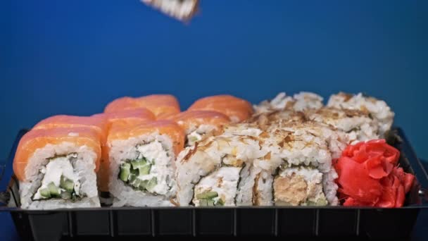 箸は寿司箱に寿司を1つ入れ 閉じます プラスチック製の箱の中で転がる デリバリーコンテナ内には様々なおいしい寿司ロールがセットになっています コンセプトアジア料理 健康的な食事 テイクアウト食事 — ストック動画
