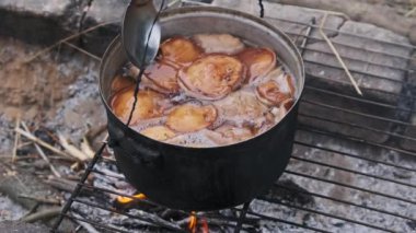 Birçok mantar bir kamp ateşinde bir tencerede pişirilir. Mantarlar, doğada kendi kendini yetiştirmiş bir ocağın üzerinde açık ateşte kaynatılır. Ormanda kamp yaparken yemek pişirmek. 4K