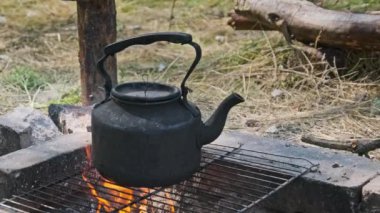 Tütsülenmiş çaydanlık, yerdeki taşlardan yapılmış kendi kendini yetiştirmiş turist ocağının üzerinde kaynar su. Doğada bir turist kamp ateşinin üzerinde duran eski bir çaydanlık. Ormanda şenlik ateşinde çay yapmak.