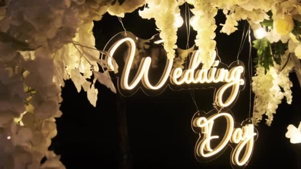 式典で結婚式の日のネオン碑文 結婚式のアーチは新鮮な白い花で飾られ 夜には電球によって照らされます 写真ゾーン スムーズなカメラムーブメント — ストック動画