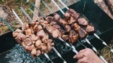 Şişler üzerindeki şiş kebaplar doğadaki ızgarada pişirilir. Kızarmış sulu domuz eti, mangalda metal şişte kızartılıyor, yakın plan. Yaz pikniğinde mangal kömürlü ve dumanlı. 4K