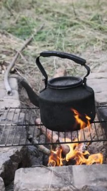 Dikey, Eski çaydanlık doğada bir turist kamp ateşinin üzerinde duruyor. İs dumanı ile kararmış çaydanlık, yerdeki taşlardan yapılmış kendi kendini yetiştirmiş turist ocağının üzerinde kaynıyor. Açık ateşte çay yapmak.