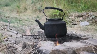 Tütsülenmiş çaydanlık, yerdeki taşlardan yapılmış kendi kendini yetiştirmiş turist ocağının üzerinde kaynar su. Doğada bir turist kamp ateşinin üzerinde duran eski bir çaydanlık. Ormanda şenlik ateşinde çay yapmak.