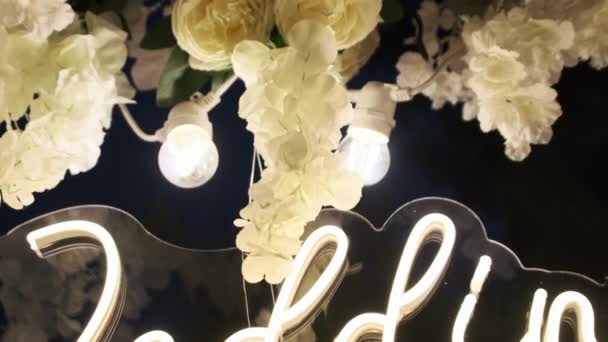 式典で結婚式の日のネオン碑文と結婚式のアーチ 休日の構成は新鮮な白い花で装飾され 夜間に電球によって照らされます スムーズなカメラの動き — ストック動画