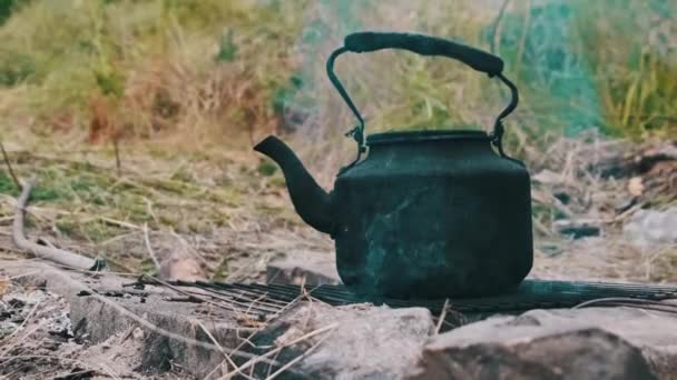 老水壶矗立在自然的旅游篝火上 被烟尘熏黑的茶壶在土里用石头做的人造旅游炉上沸腾着 在篝火上泡茶 — 图库视频影像