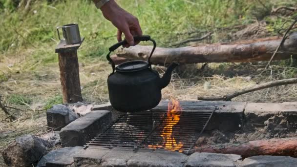 煤烟水壶是用石子铺在地面上的自制旅游炉上的开水 一个游客从火中抢了一个茶壶 古老的水壶矗立在自然的旅游篝火上 — 图库视频影像