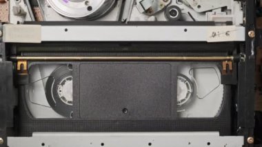 VHS video kasedi VCR kaydedicinin içine koyuldu ve oynatılıyor. Video kasetin klasik VHS mekanizması video başına bant takar. İçerideki eski video kaydedici. Eski video dosyası veya film çalma kavramı.