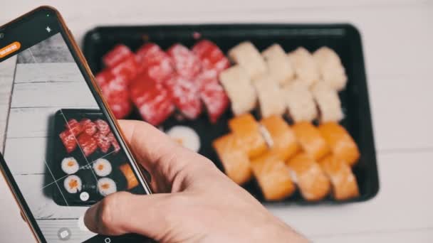 ブログでは Snsに投稿するためのスマートフォンカメラで寿司ロールの動画を撮影しています 携帯電話の宅配プラスチック製の箱で日本食を撮影する男性の手 ソーシャルメディアのための撮影 — ストック動画
