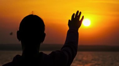 Genç bir kızın silueti gün batımına doğru uzanır, ağır çekimde. Kadın elinin arasına güneş ışınları yerleştiriyorum. Güneşte bir avuç, Tanrı 'ya inanmak. Hayal, mutluluk, özgürlük, zihinsel sağlık