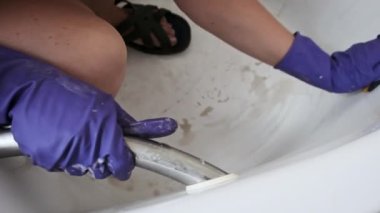 Kirli tuvaleti turuncu süngerle yavaş çekimde temizleyen bir kadın. Mavi lastik eldivenli kadın elleri banyoyu siliyor. Küvet yüzeyini deterjanlarla temizliyorum. Ev işi, temizlik konsepti