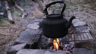 Tütsülenmiş çaydanlık, yerdeki taşlardan yapılmış kendi kendini yetiştirmiş turist ocağının üzerinde kaynar su. Doğada bir turist kamp ateşinin üzerinde duran eski bir çaydanlık. Ormanda şenlik ateşinde çay yapmak.