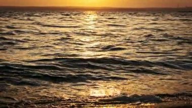 Gün batımında su yüzeyinde ağır çekimde. Batan güneşte altın renkli dalgaların güzel arkaplanı. Güneş ışınlarının su yüzeyine yansıması. Dalgaların üzerinde gün batımı. Dalgalar kıyıya vuruyor