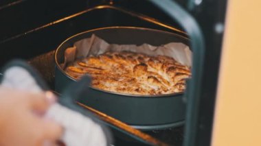 Fırında ev yapımı turta pişirmek. Mutfaktaki fırından kek tepsisi ve elmalı kek çeken kadın elleri, yakın plan. Ev hanımı yemek hazırlıyor. Tatlı tatlı. 4K