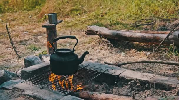 火の上にティーポット 古いヴィンテージのスモークケトルは 地面に石で作られた自家製の観光用ストーブの上に沸騰した水です キャンプ近くの森でボンファイアでお茶を作る クローズアップ — ストック動画