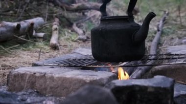 Eski çaydanlık doğada bir turist kamp ateşinin üzerinde duruyor. İs dumanı ile kararmış çaydanlık, yerdeki taşlardan yapılmış kendi kendini yetiştirmiş turist ocağının üzerinde kaynıyor. Açık ateşte çay yapmak.