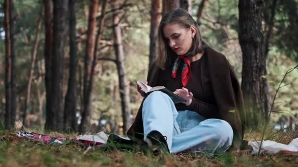 여자는 소나무 숲에서 담요에 읽습니다 메이크업과 귀여운 독서를 즐긴다 자연에서 — 비디오