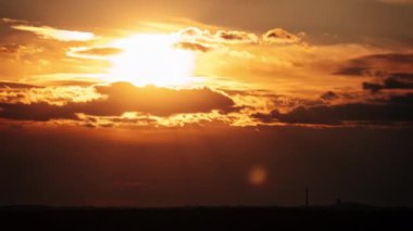 Turuncu gökyüzünde bulutlarla hareket eden muhteşem gün batımı zamanı. Parlak turuncu güneş ufuk çizgisinde katmanlı bulutların arkasında hareket ediyor. Destansı bulut uzayı, canlı bir renk. Zaman aşımı. Gün batımı 4K