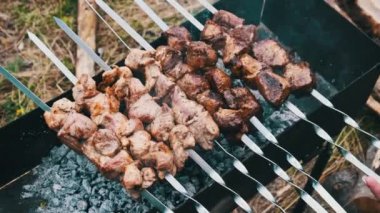 Şişler üzerindeki şiş kebaplar doğadaki ızgarada pişirilir. Kızarmış sulu domuz eti, mangalda metal şişte kızartılıyor, yakın plan. Yaz pikniğinde mangal kömürlü ve dumanlı. 4K